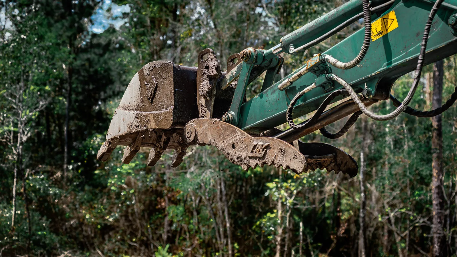 Excavator bucket and thumb raised over a wooded lot, land clearing