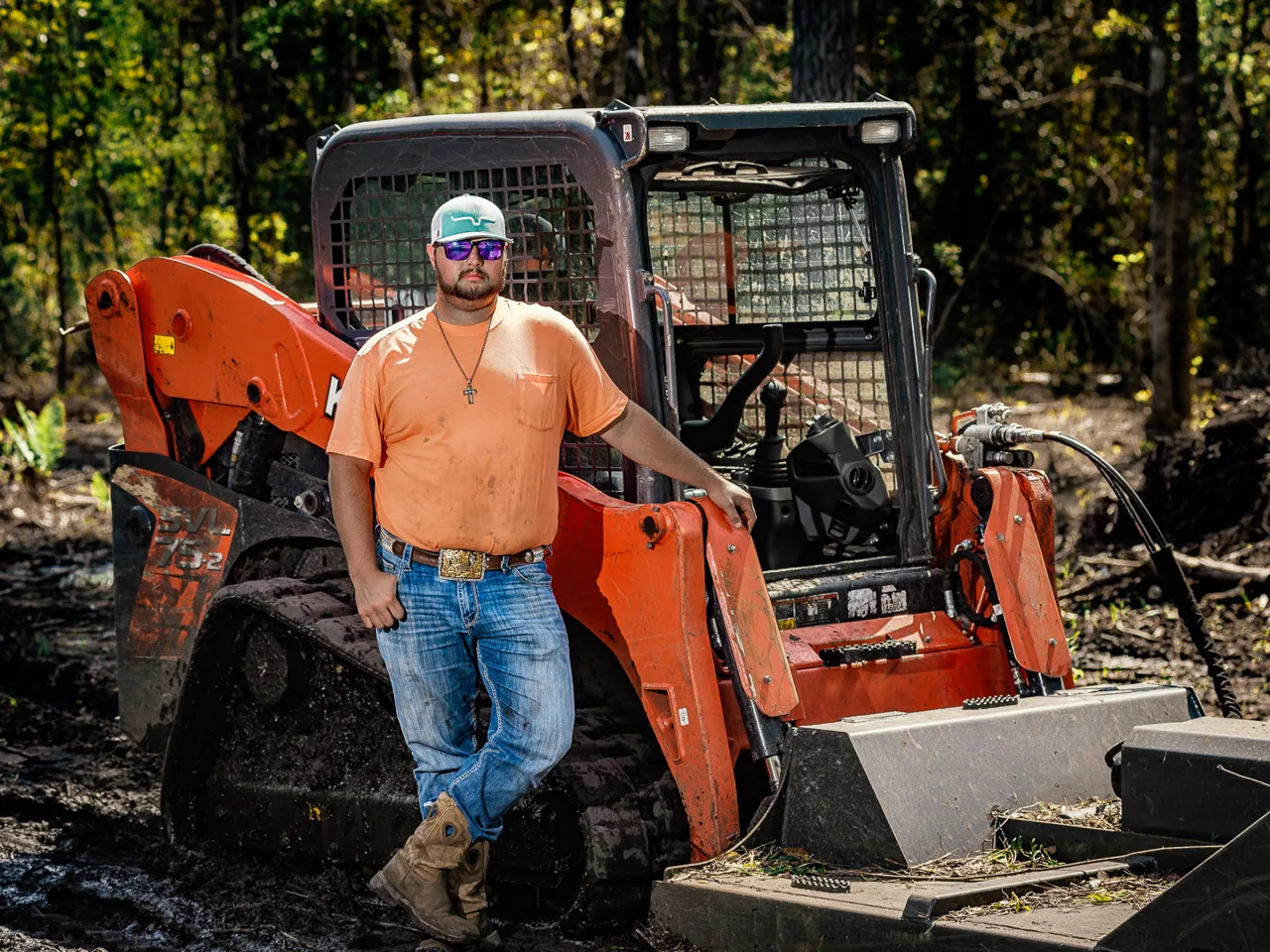 Crew member leaning on a track loader with a brush mower deck in the woods, land clearing
