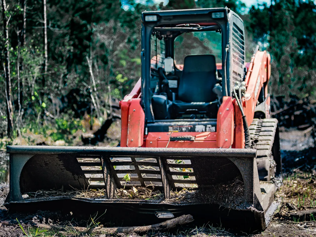 Front of a track loader with a brush mower deck on cut brush in the woods, brush mowing