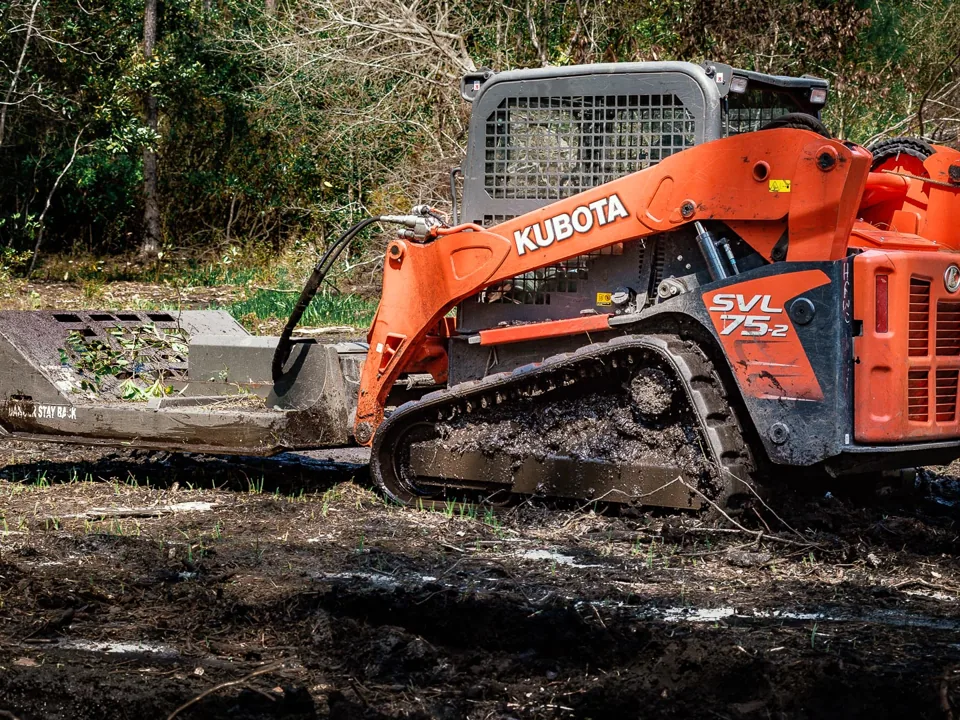 Track loader with a brush mower deck on freshly cut ground at the edge of the woods, brush mowing