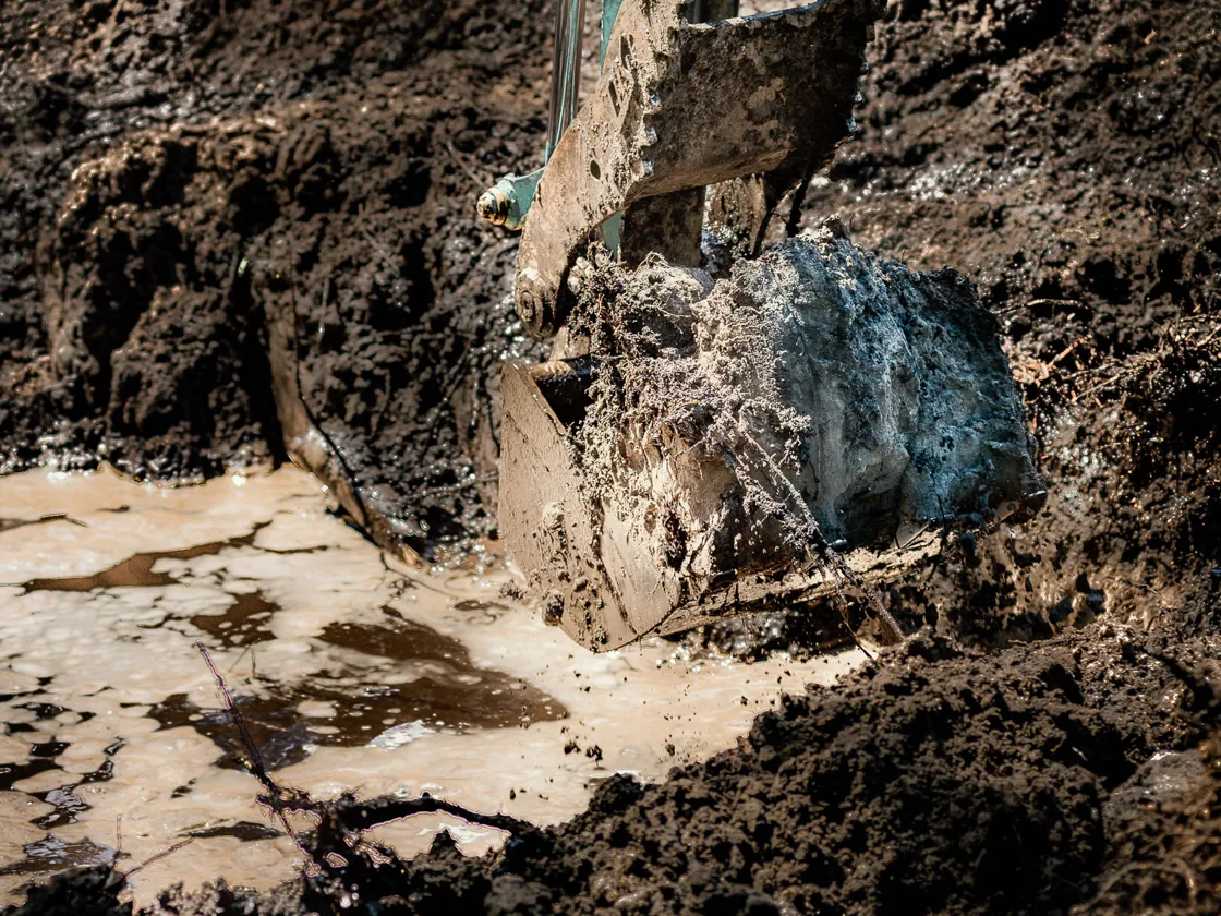 Excavator bucket lifting wet clay out of a flooded dig, excavating
