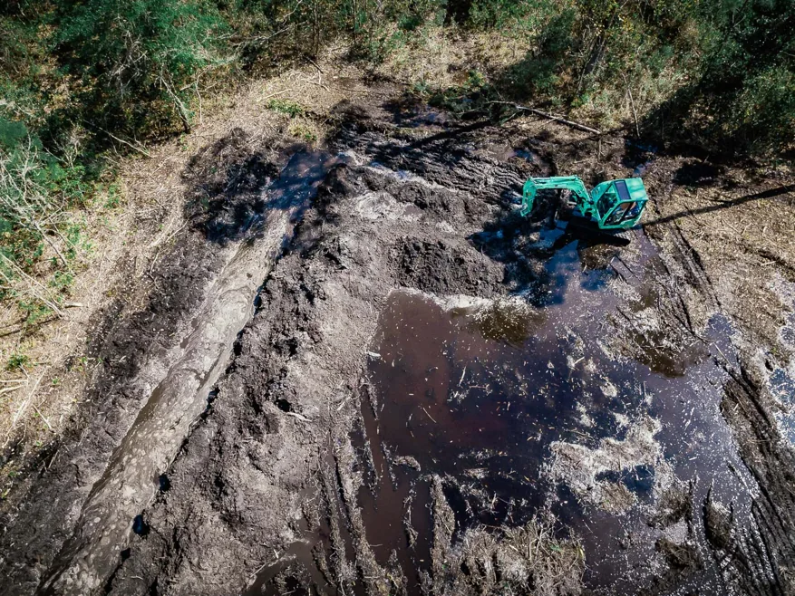 Overhead view of an excavator shaping a new pond with water filling the dig, excavating