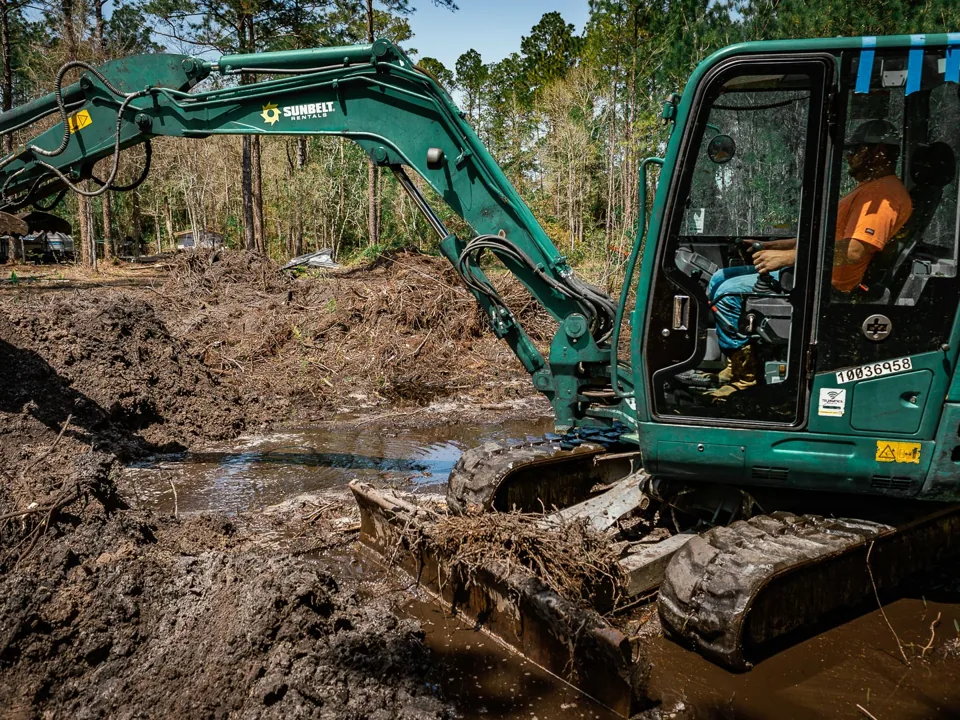 Excavator digging a pond in wet ground with cleared brush piled behind, excavating