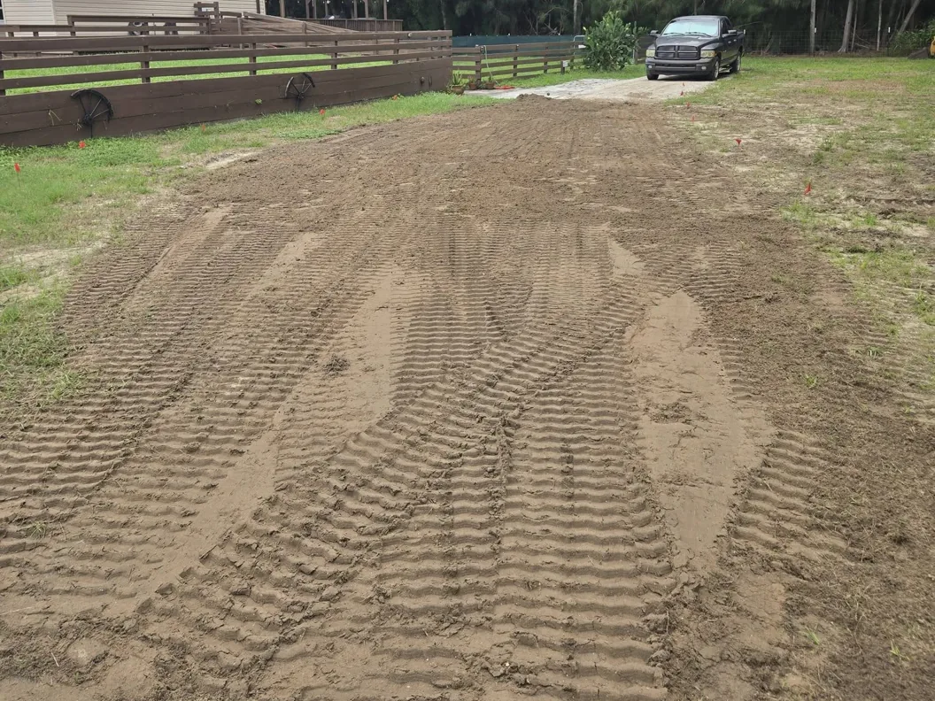Graded dirt driveway base with marker flags along a board fence, gravel driveways