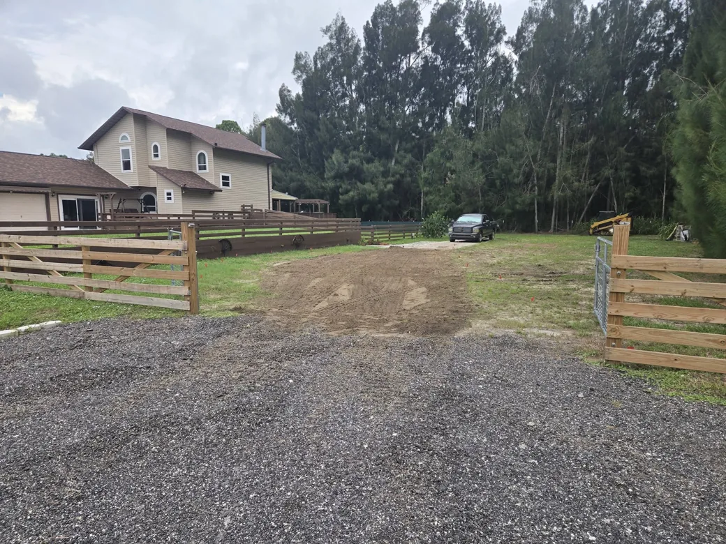 Gravel apron and a freshly graded drive running through a new board fence gate, gravel driveways