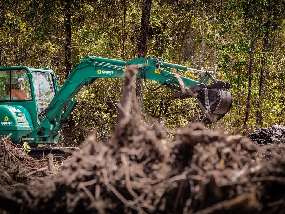 Excavator behind a pile of pulled roots and stumps on a cleared lot, land clearing