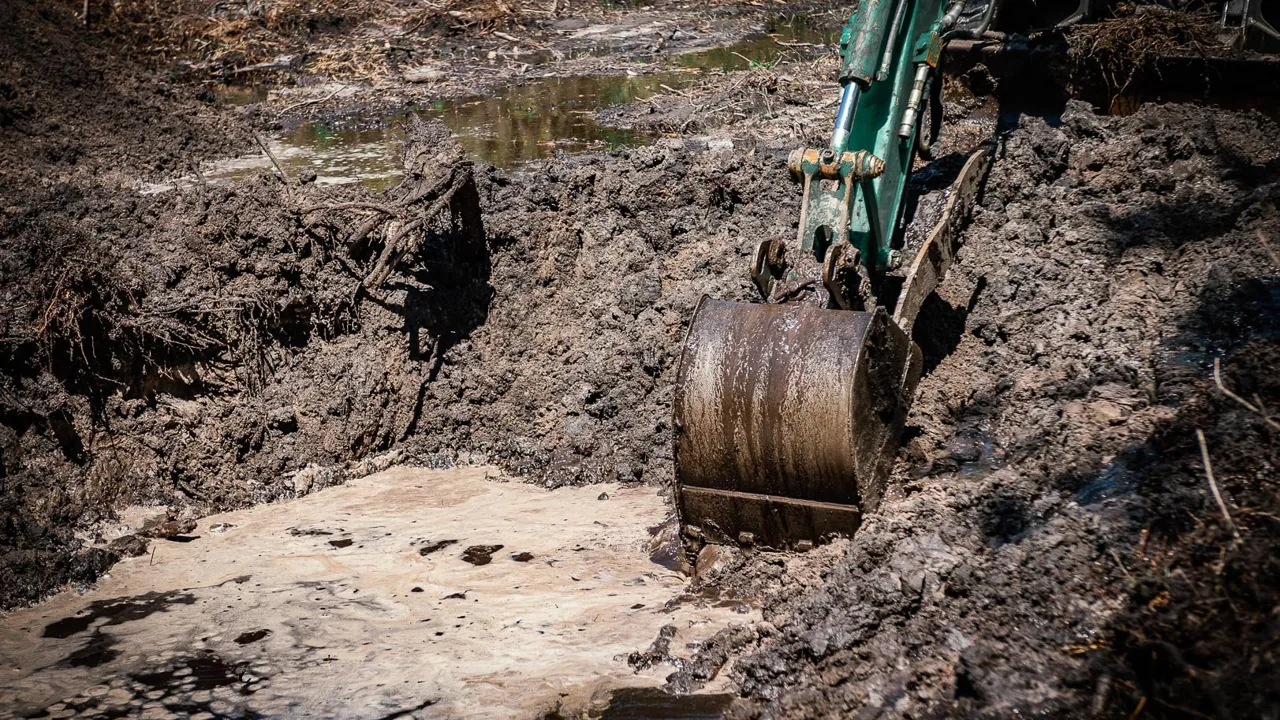 Excavator bucket digging into the bank of a flooded pond dig, land clearing