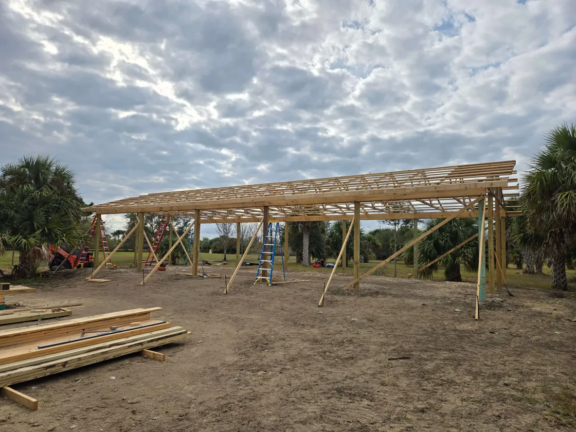 Pole barn shell going up on a cleared pad, posts and roof purlins in place