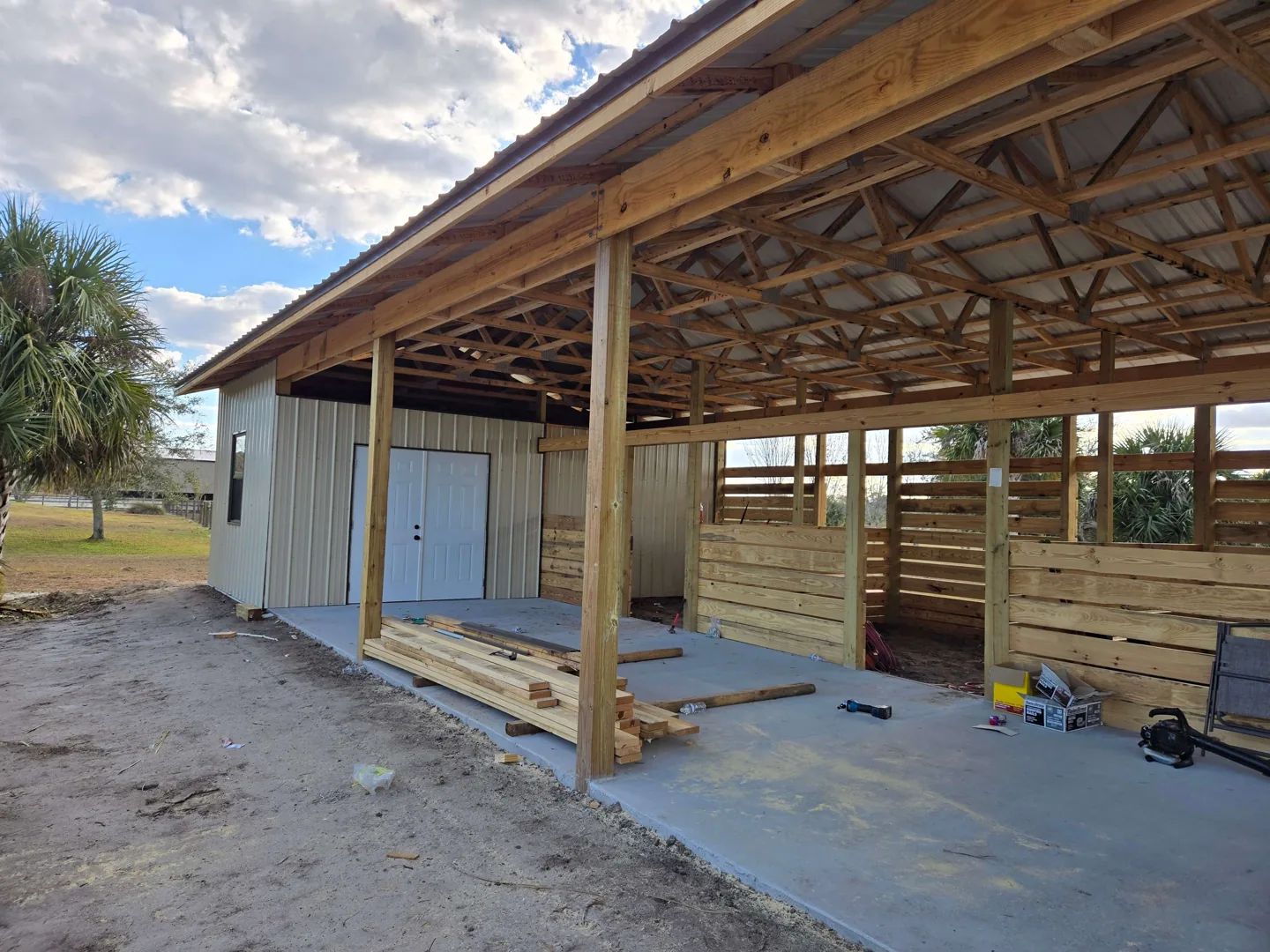 Pole barn with a metal roof over wood trusses, a closed tack room and board stall walls, pole barns