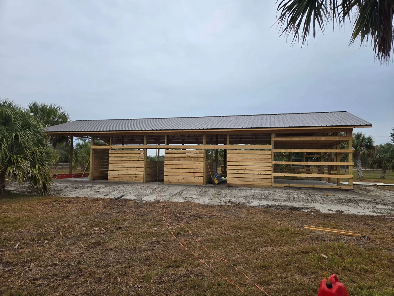 Long pole barn with a new metal roof and board walls between the posts, pole barns