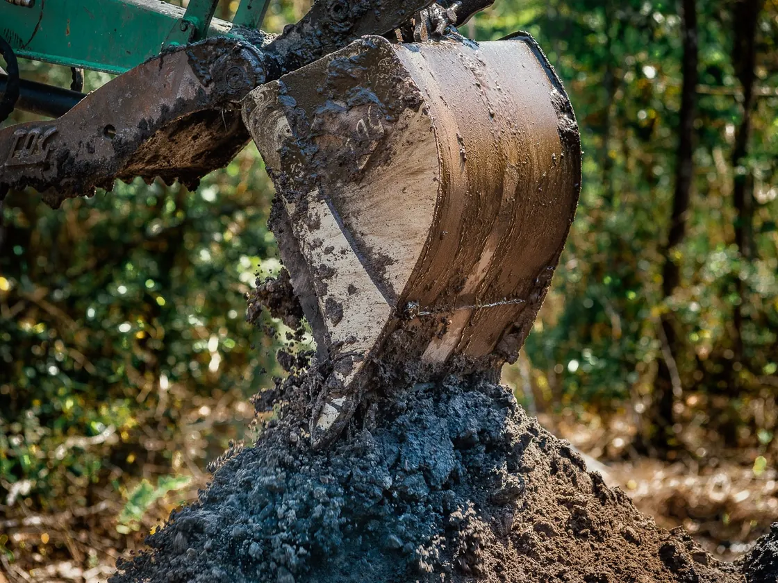 Excavator bucket dropping wet sand on the spoil pile beside a pond dig, pond construction