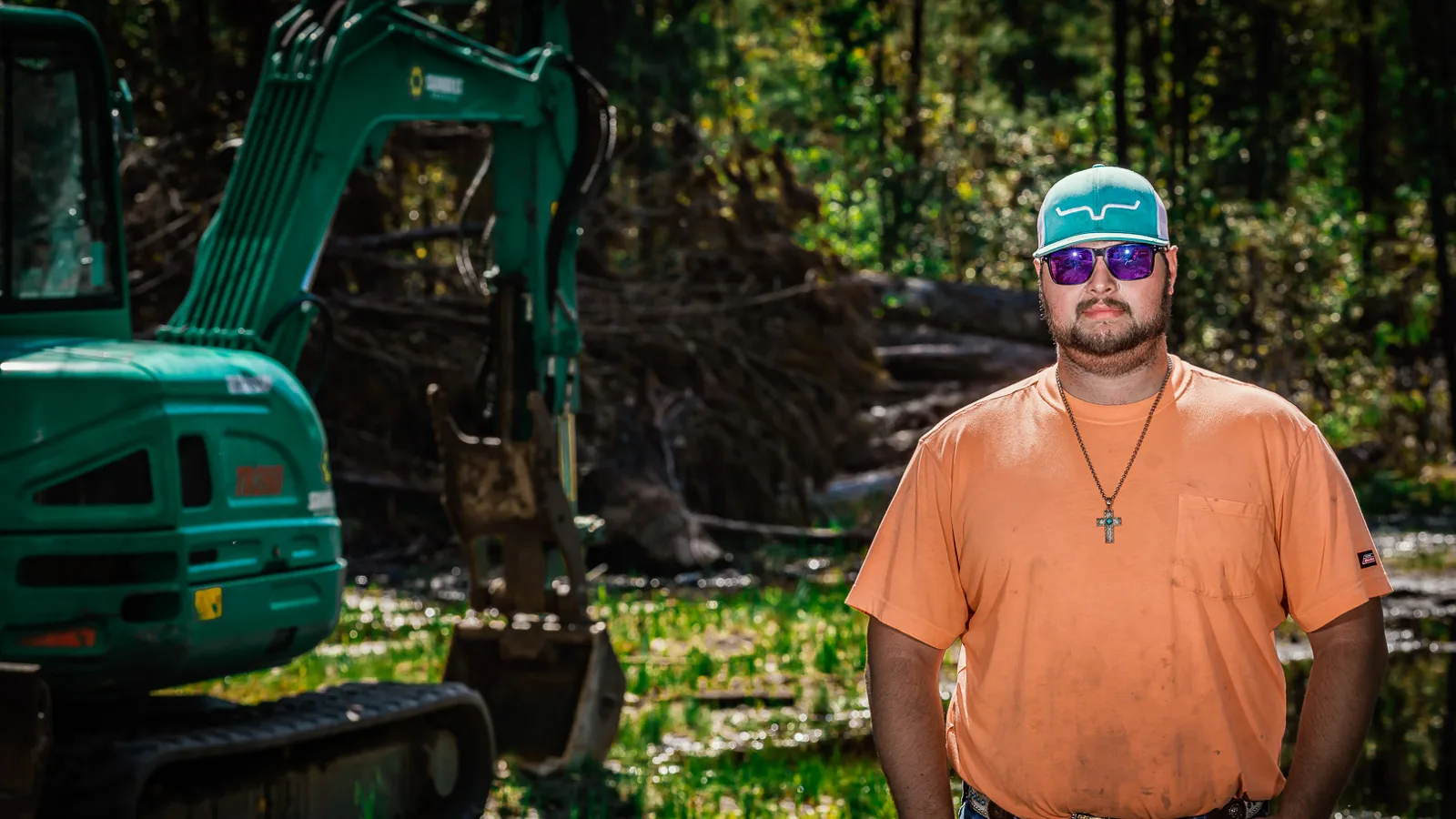 Crew member standing beside an excavator on a cleared wooded lot, land clearing